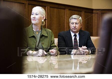 Stock Photography - Business people sitting by conference table and looking away in an office. Fotosearch