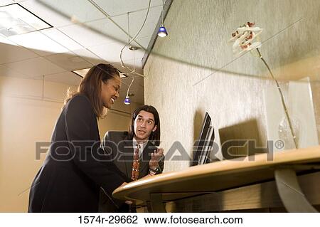 Stock Image - Businessman and businesswoman looking at a computer monitor in an office. Fotosearch