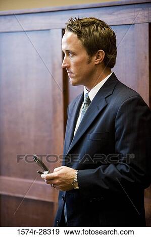 Businessman holding a mobile phone in an office View Large Photo Image Stock Photo - Businessman holding a mobile phone in an office. Fotosearch