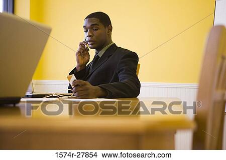 Businessman in full suit using mobile phone and laptop in an office View Large Photo Image Picture - Businessman in full suit using mobile phone and laptop in an office. Fotosearch