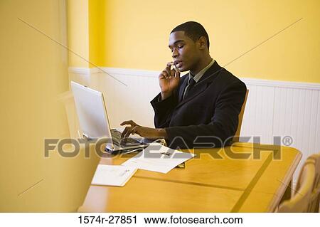 Businessman in full suit using mobile phone and laptop in an office View Large Photo Image Stock Image - Businessman in full suit using mobile phone and laptop in an office. Fotosearch