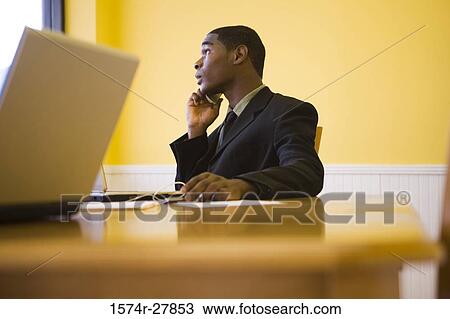 Businessman in full suit using mobile phone and laptop in an office View Large Photo Image Stock Image - Businessman in full suit using mobile phone and laptop in an office. Fotosearch