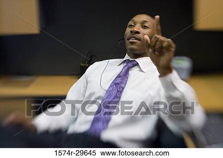 Businessman sitting and pointing upward in an office View Large Photo Image Stock Photography - Businessman sitting and pointing upward in an office. Fotosearch