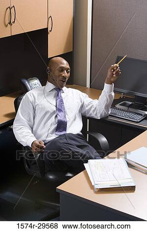 Stock Photo - Businessman sitting by a computer and pointing upward in an office. Fotosearch