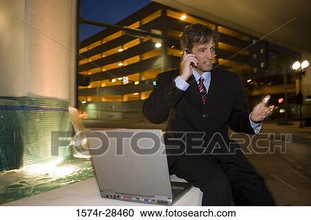 Businessman sitting by laptop and communicating on mobile phone View Large Photo Image Stock Image - Businessman sitting by laptop and communicating on mobile phone. Fotosearch
