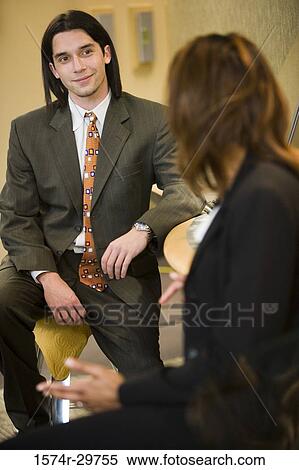 Businessman sitting by table with colleague in an office View Large Photo Image Stock Photography - Businessman sitting by table with colleague in an office. Fotosearch