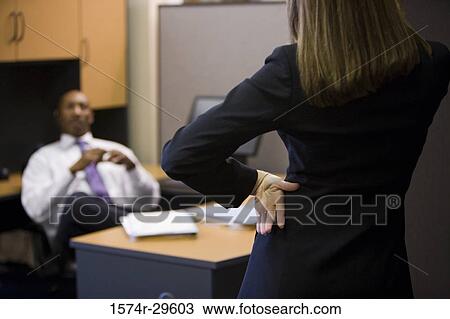 Businessman sitting while businesswoman standing in front of him in an office View Large Photo Image Stock Image - Businessman sitting while businesswoman standing in front of him in an office. Fotosearch
