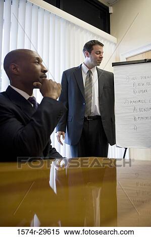Businessman sitting with hand on chin by colleague in an office View Large Photo Image Stock Photography - Businessman sitting with hand on chin by colleague in an office. Fotosearch
