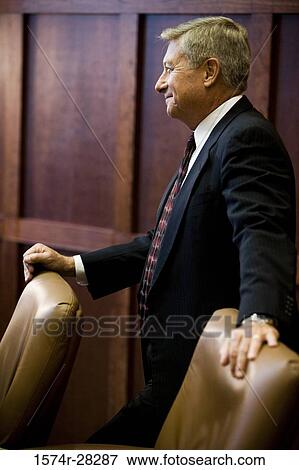 Businessman standing by armchairs and smiling in an office View Large Photo Image Stock Photo - Businessman standing by armchairs and smiling in an office. Fotosearch