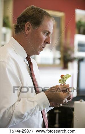 Stock Photo - Businessman standing in the kitchen and holding salad in the bowl. Fotosearch