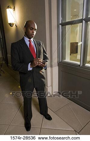 Businessman standing out of an office and using a mobile phone View Large Photo Image Stock Photograph - Businessman standing out of an office and using a mobile phone. Fotosearch
