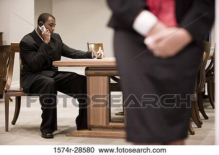 Businessman using a mobile phone while businesswoman standing in an office View Large Photo Image Stock Image - Businessman using a mobile phone while businesswoman standing in an office. Fotosearch