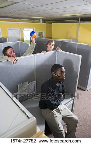 Stock Image - Businessman using headset while colleagues holding ball in an office. Fotosearch