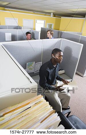 Businessman using headset while colleagues conversing in the background View Large Photo Image Stock Photo - Businessman using headset while colleagues conversing in the background. Fotosearch