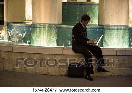 Businessman using laptop computer by fountain View Large Photo Image Stock Photo - Businessman using laptop computer by fountain. Fotosearch