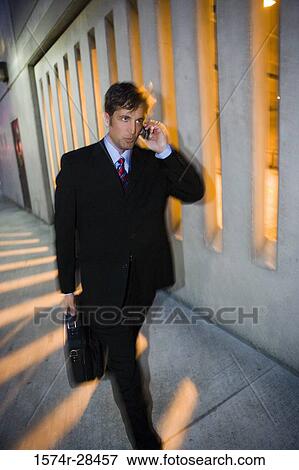 Businessman walking on sidewalk and communicating on mobile phone View Large Photo Image Stock Photo - Businessman walking on sidewalk and communicating on mobile phone. Fotosearch
