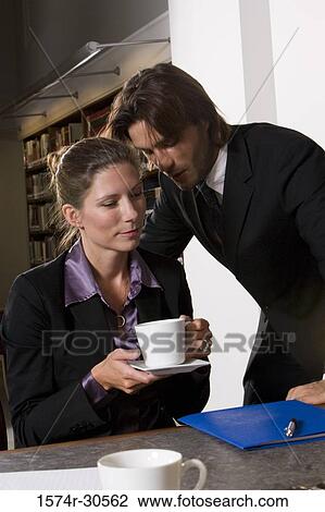 Stock Image - Businessman whispering to businesswoman in an office. Fotosearch