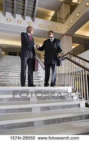 Stock Image - Businessmen handshaking on staircase in an office. Fotosearch