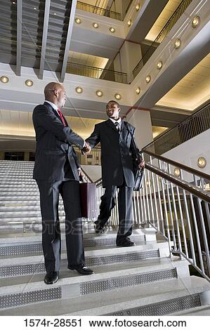 Businessmen handshaking on staircase in an office View Large Photo Image Stock Image - Businessmen handshaking on staircase in an office. Fotosearch