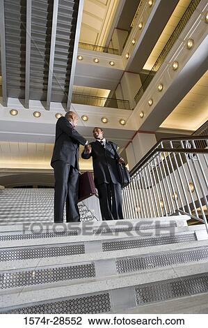 Stock Image - Businessmen handshaking on staircase in an office. Fotosearch