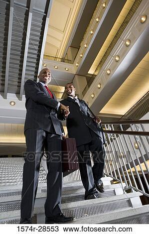 Businessmen handshaking on staircase in an office View Large Photo Image Stock Image - Businessmen handshaking on staircase in an office. Fotosearch