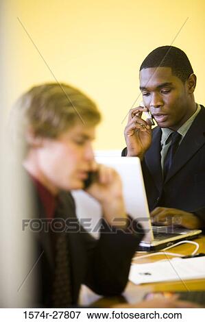 Businessmen in full suit using mobile phone and laptop in an office View Large Photo Image Stock Photo - Businessmen in full suit using mobile phone and laptop in an office. Fotosearch