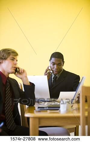 Businessmen in full suit using mobile phone and laptop in an office View Large Photo Image Stock Photo - Businessmen in full suit using mobile phone and laptop in an office. Fotosearch