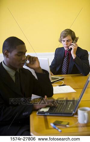 Businessmen in full suit using mobile phone and laptop in an office View Large Photo Image Stock Photograph - Businessmen in full suit using mobile phone and laptop in an office. Fotosearch