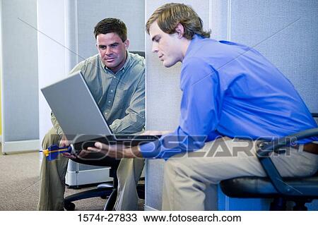 Stock Image - Businessmen looking at laptop in an office. Fotosearch