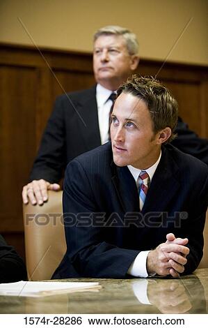Businessmen looking away by conference table in an office View Large Photo Image Stock Photograph - Businessmen looking away by conference table in an office. Fotosearch