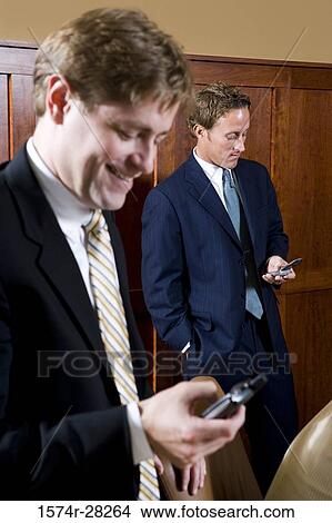 Businessmen text messaging on mobile phone in an office View Large Photo Image Picture - Businessmen text messaging on mobile phone in an office. Fotosearch