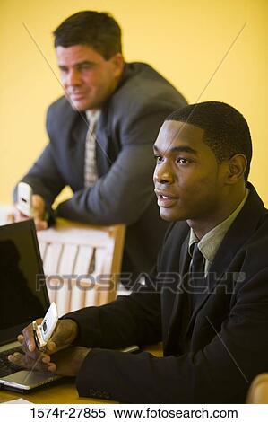Businessmen using mobile phone and laptop in an office View Large Photo Image Stock Photography - Businessmen using mobile phone and laptop in an office. Fotosearch