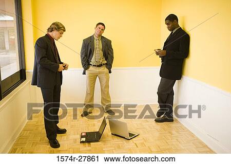 Stock Image - Businessmen using mobile phones in an office. Fotosearch