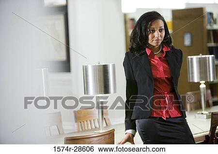 Stock Photograph - Businesswoman leaning by conference table in an office. Fotosearch