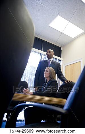 Stock Photo - Businesswoman sitting by a businessman standing in an office. Fotosearch