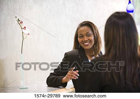 Businesswoman sitting by a colleague in an office View Large Photo Image Stock Photo - Businesswoman sitting by a colleague in an office. Fotosearch