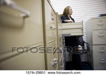 Stock Image - Businesswoman standing by lockers in an office. Fotosearch
