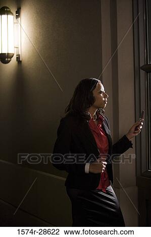 Stock Image - Businesswoman standing out of an office and using a mobile phone. Fotosearch