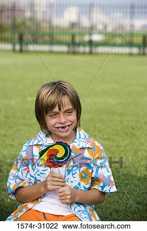 Cheerful boy sitting on grass and holding lollipop View Large Photo Image Stock Image - Cheerful boy sitting on grass and holding lollipop. Fotosearch