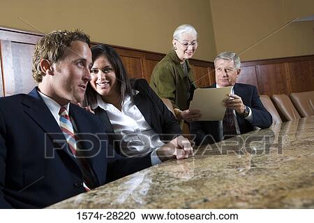 Stock Image - Cheerful business people discussion by conference table in an office. Fotosearch