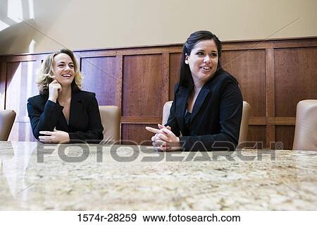 Cheerful business people sitting by conference table in an office View Large Photo Image Stock Photo - Cheerful business people sitting by conference table in an office. Fotosearch