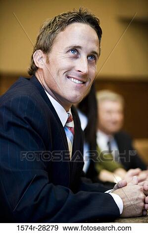Cheerful businessman looking up while colleagues in the background View Large Photo Image Stock Photo - Cheerful businessman looking up while colleagues in the background. Fotosearch
