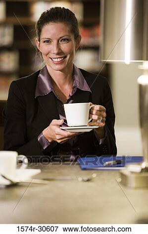 Cheerful businesswoman holding a tea cup in an office View Large Photo Image Stock Photo - Cheerful businesswoman holding a tea cup in an office. Fotosearch