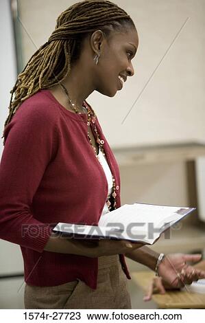 Cheerful female teacher holding book and standing in the classroom View Large Photo Image Stock Image - Cheerful female teacher holding book and standing in the classroom. Fotosearch