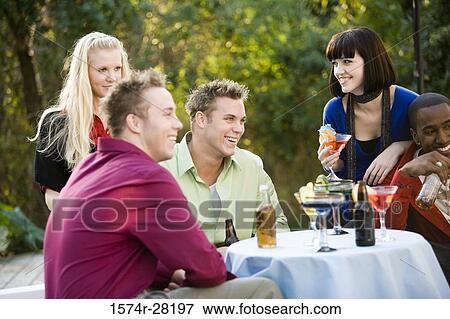 Cheerful friends enjoying drinks around table View Large Photo Image Stock Photo - Cheerful friends enjoying drinks around table. Fotosearch