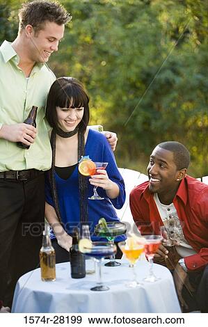 Cheerful friends enjoying drinks by table View Large Photo Image Stock Photo - Cheerful friends enjoying drinks by table. Fotosearch