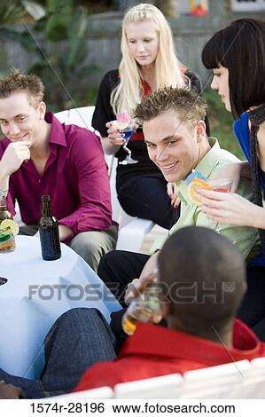 Cheerful friends enjoying drinks by table View Large Photo Image Stock Photograph - Cheerful friends enjoying drinks by table. Fotosearch