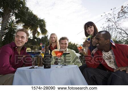 Cheerful friends enjoying wines by table View Large Photo Image Stock Image - Cheerful friends enjoying wines by table. Fotosearch