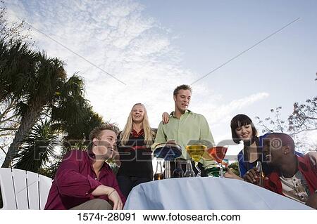 Cheerful friends enjoying wines by table View Large Photo Image Stock Image - Cheerful friends enjoying wines by table. Fotosearch