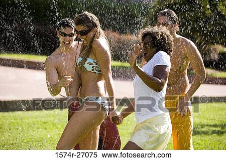 Stock Photography - Cheerful friends enjoying with water sprinkler on lawn. Fotosearch